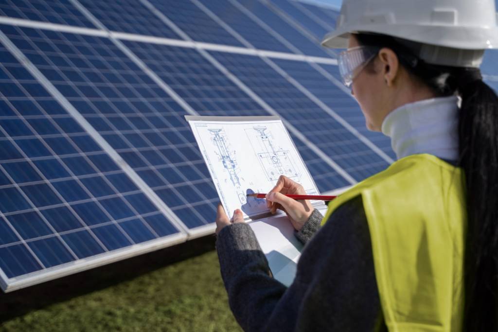 Teknisyen, güvenlik ekipmanı kullanarak güneş enerji sistemlerinde bakım çalışması yaparken, çatıda monte edilmiş güneş panelleri arasında detaylı kontrol gerçekleştiriyor.